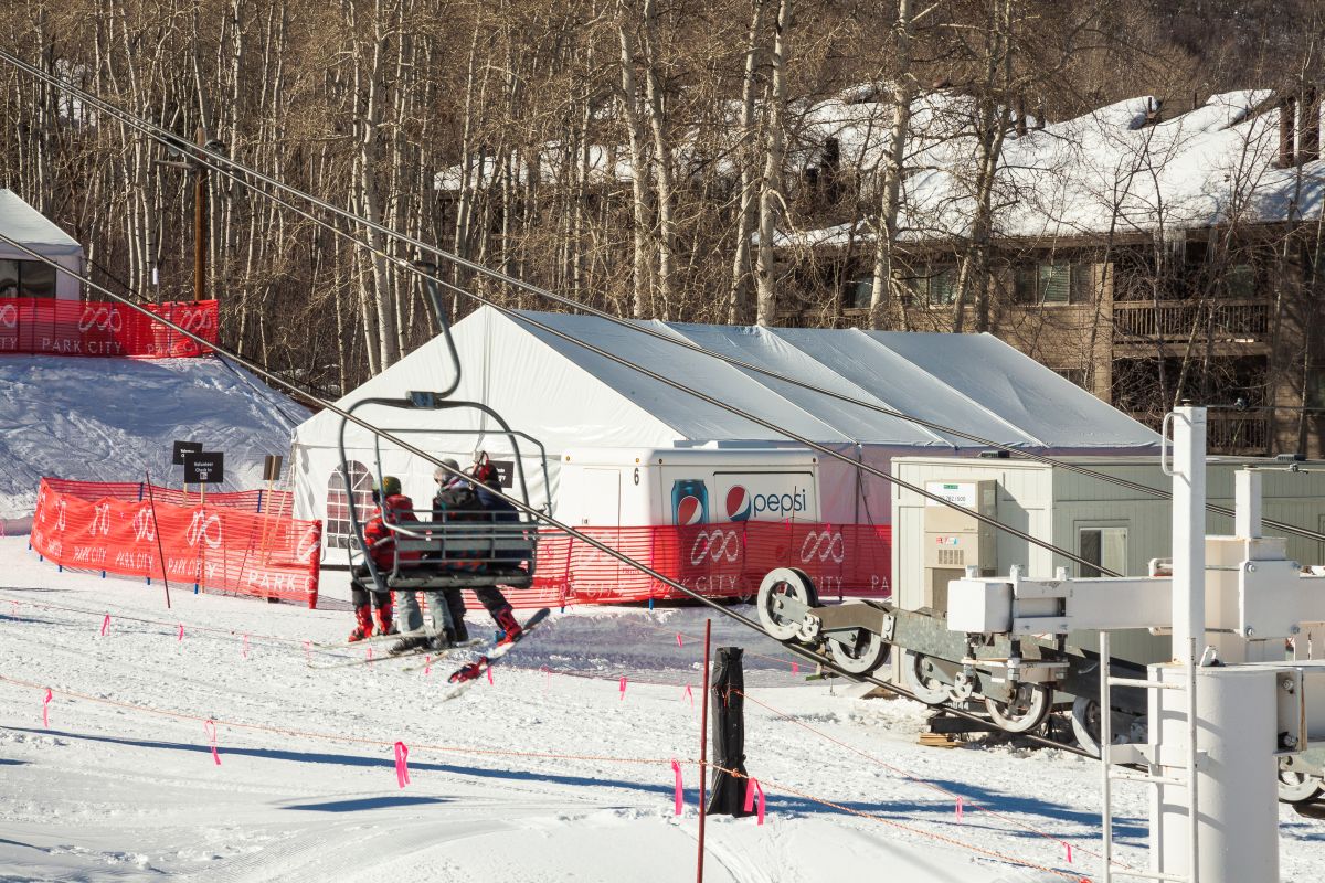 Two passengers riding the ski lift, with an enclosed tent in the background